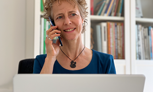 Irene de Groot, grafisch ontwerper, aan de telefoon achter een laptop